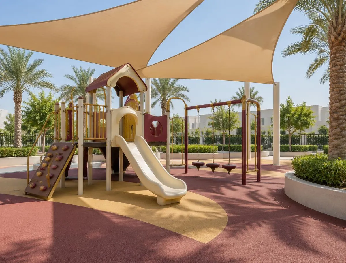 A safe outdoor playground with a slide, swings and soft rubber flooring under large shade sails and palm trees.
